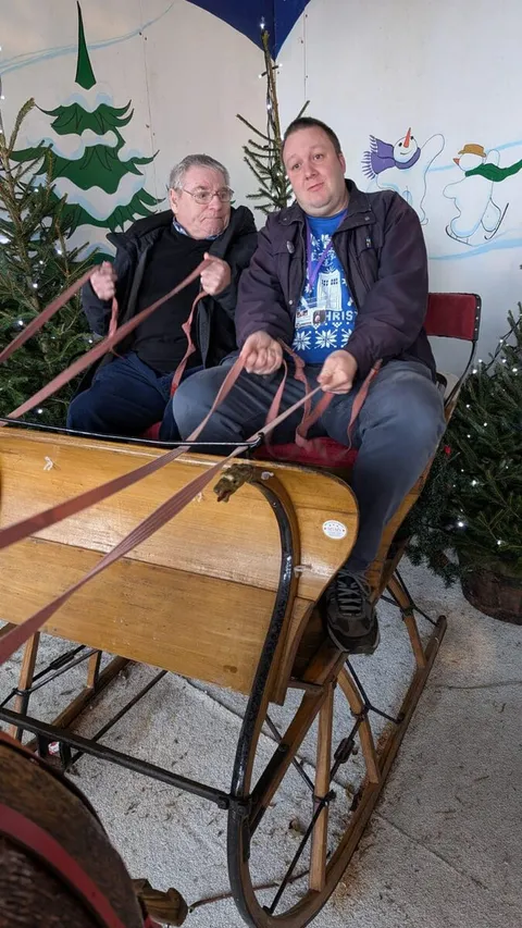 Two holidaymakers sitting in an antique wooden sleigh